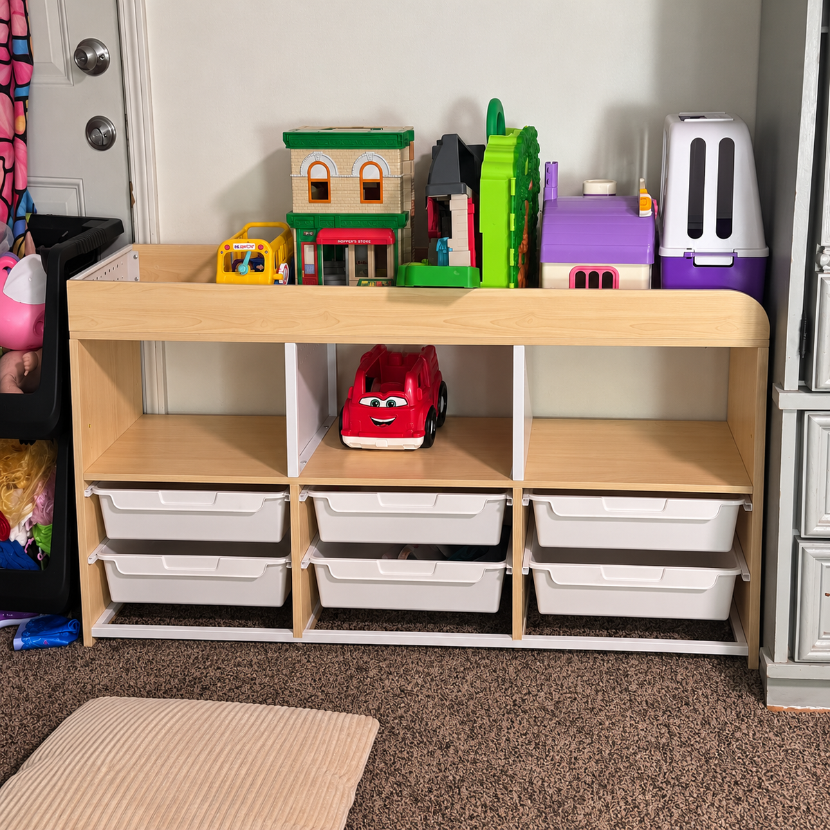 Natural wood kids storage cubbies with white drawers, toy houses and books in a playroom